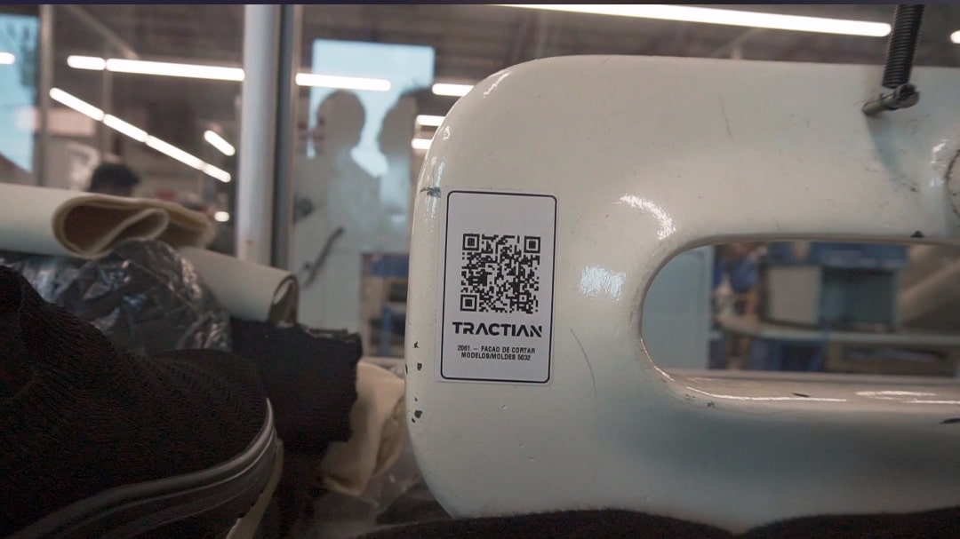 Uma máquina branca está adesivada com um QR Code, é possível ler o nome TRACTIAN no adesivo.
