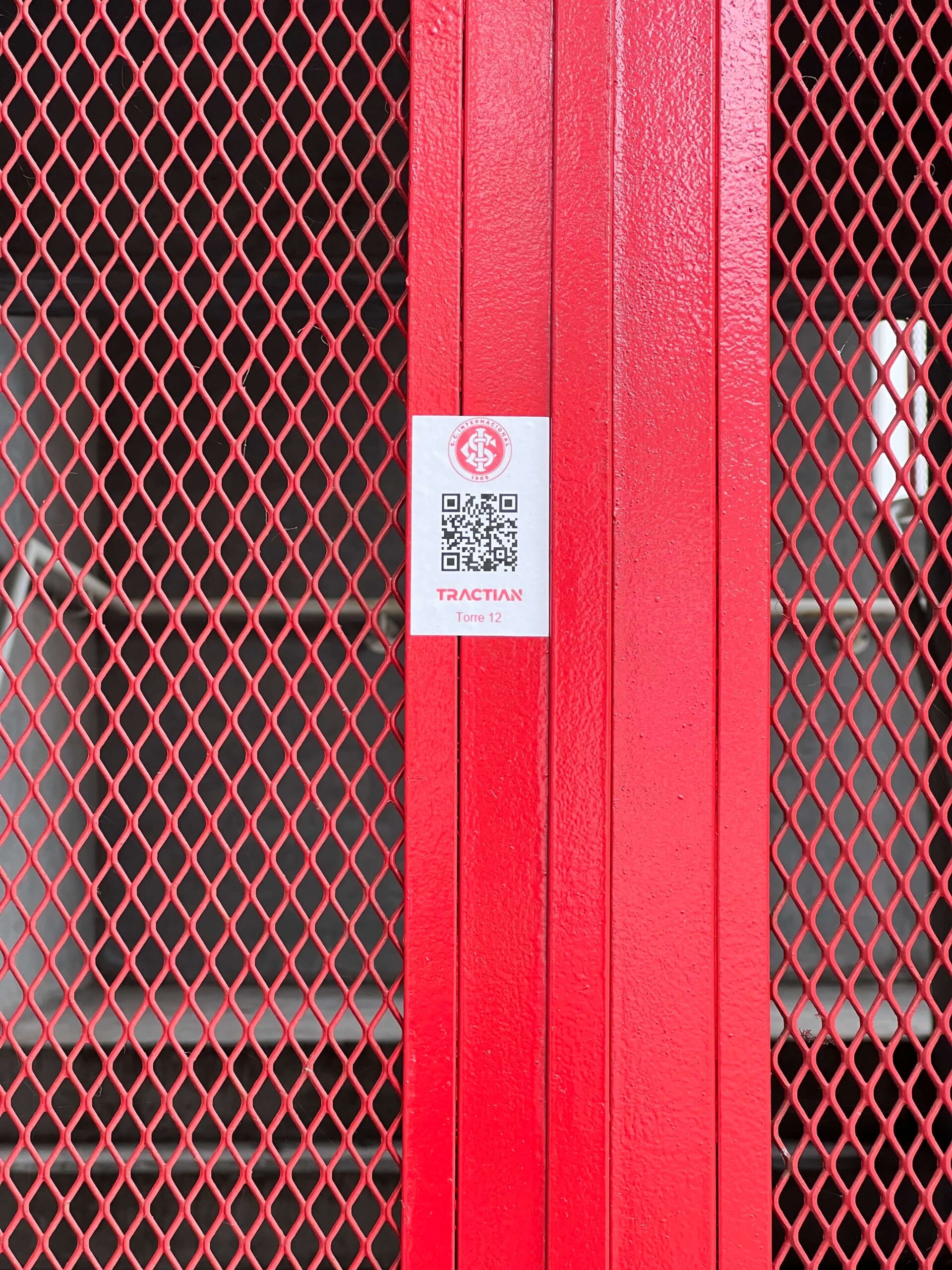 Em uma estrutura de cor vermelha, um QR Code está colado. No adesivo, a marca do Sport Club Internacional, o código QR e a identificação do local.